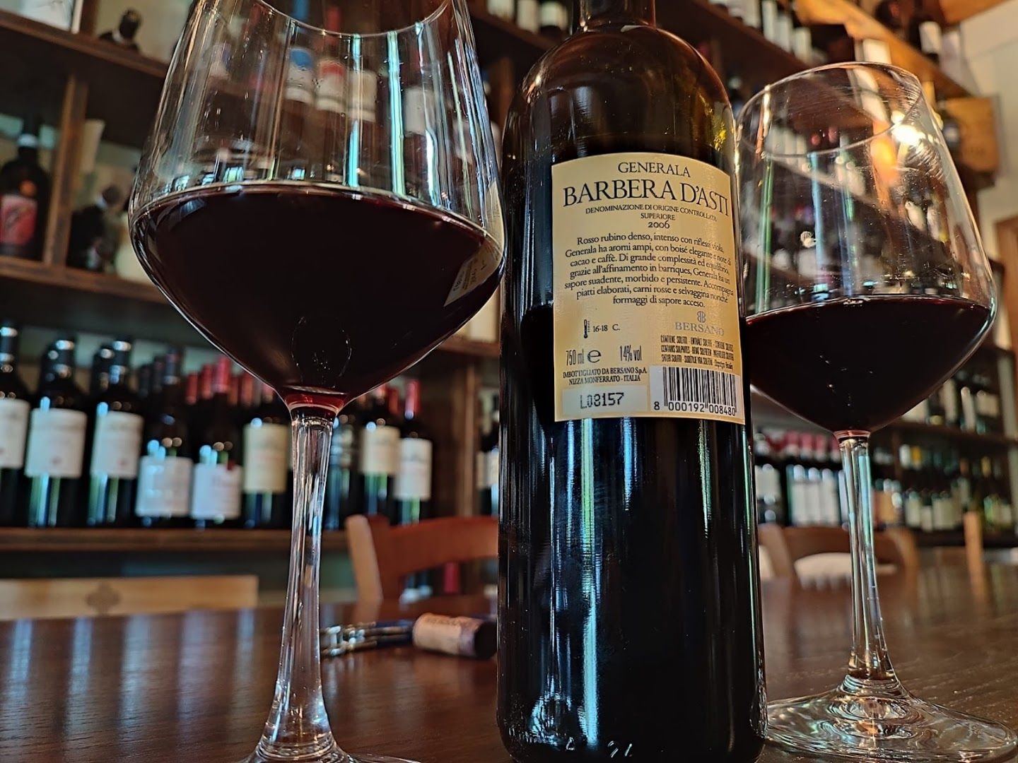 Una bottiglia di Barbera d'Asti e due calici davanti alla parete dei vini